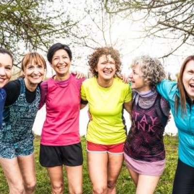 A line-up of six women standing outdoors dressed in exercise gear, smiling and with their arms around the person beside them.